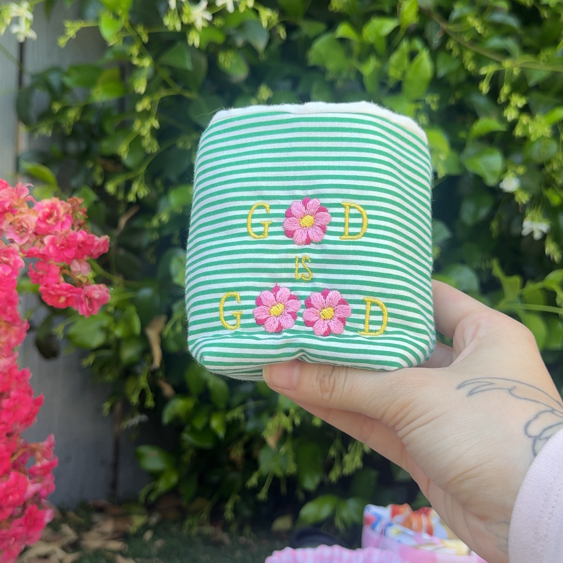 Hand holding a green striped fabric coffee drink sleeve pouch with floral designs against a natural background.