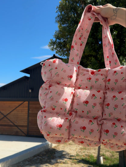 Pink floral quilted bag held outdoors with a clear blue sky and wooden building in the background