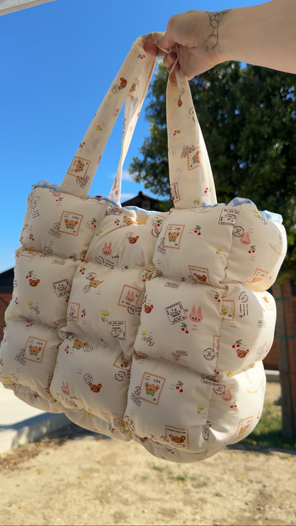 Padded quilted carry tote bag with patterned fabric held against a blue sky and trees