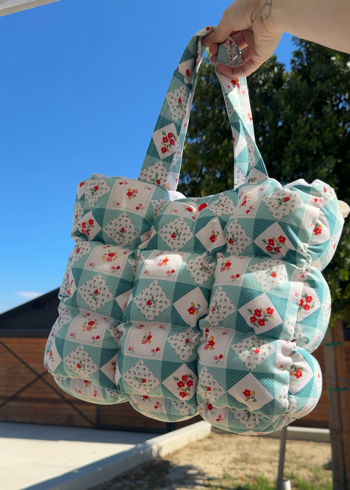 Quilted bag with floral pattern held outdoors against a blue sky.
