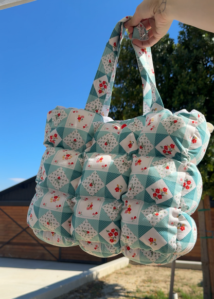 Quilted bag with floral pattern held outdoors against a blue sky.