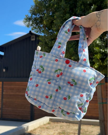 Hand holding a patterned bag against a clear blue sky with trees and a building in the background.