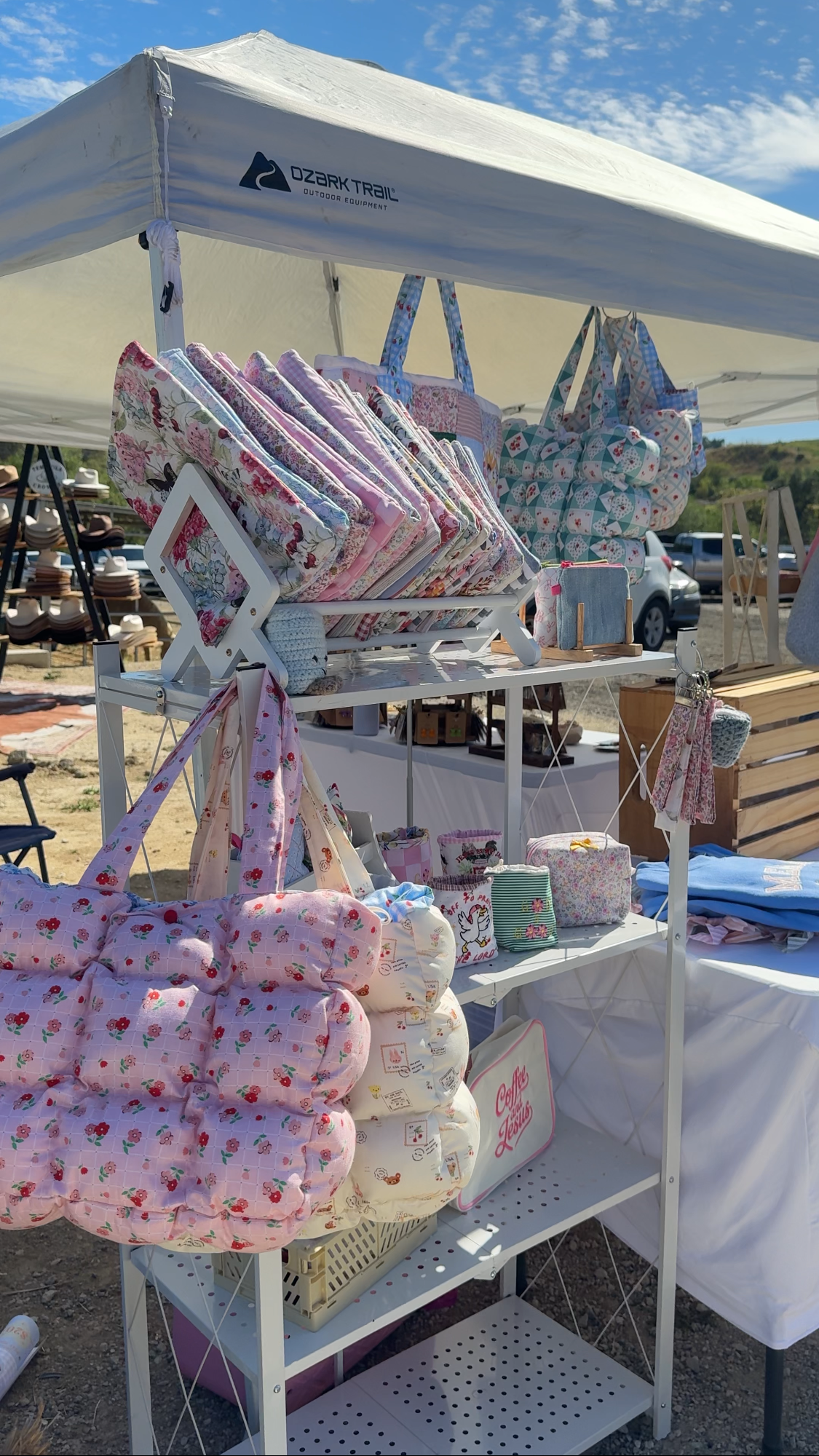 Product display with bags and items under a white tent at an outdoor market.