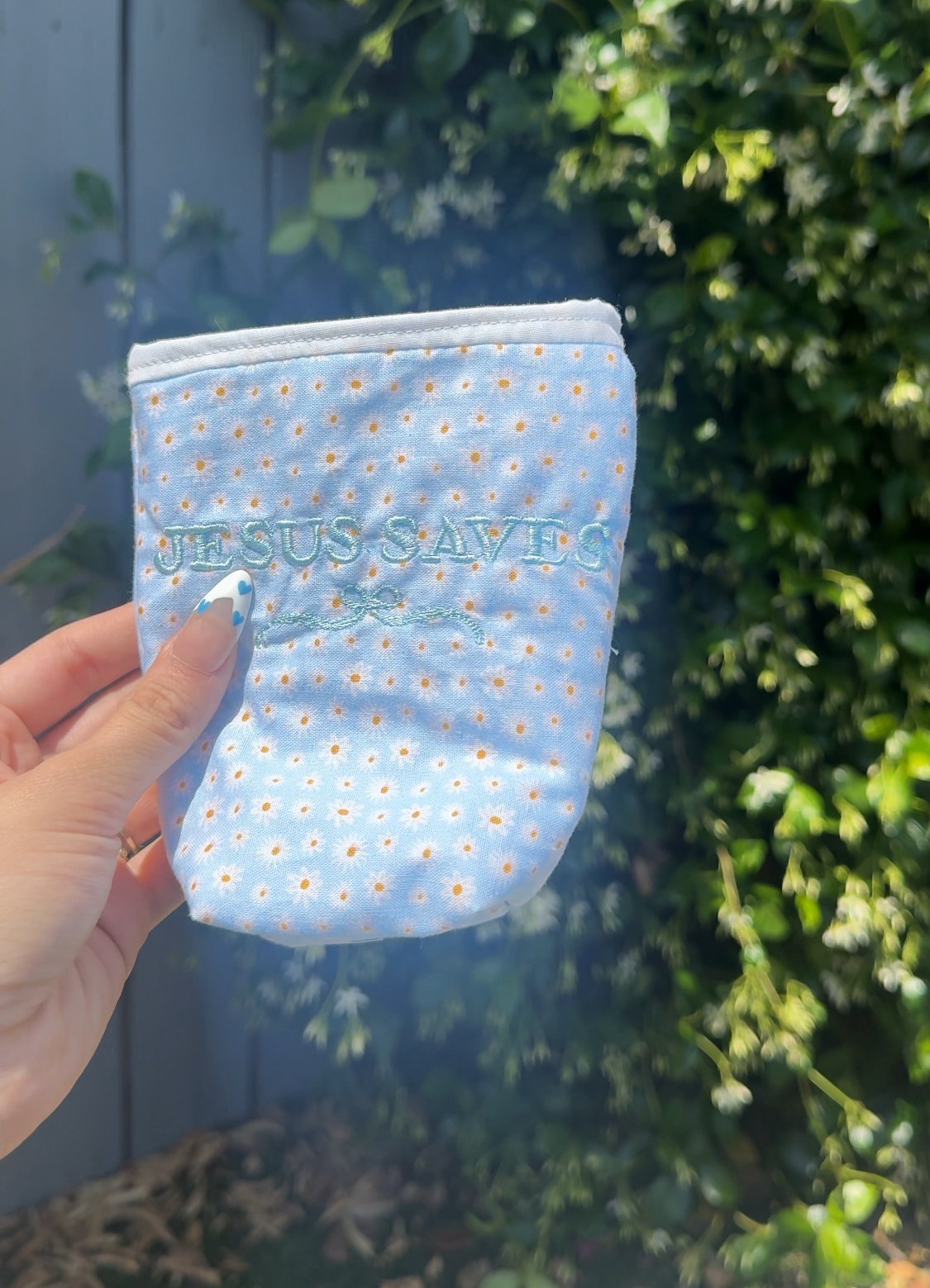 Small blue pouch with white floral pattern held in front of green foliage