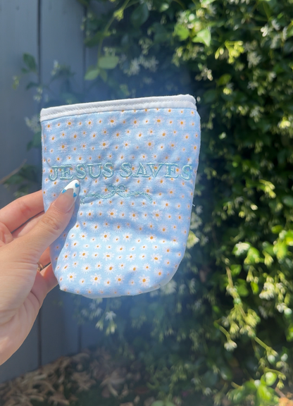 Small blue pouch with white floral pattern held in front of green foliage